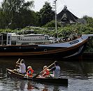 11_21585 Eine Familie paddeln in einem Kanu auf der Dove-Elbe - die Kinder tragen zur Sicherheit Schwimmwesten. Am Ufer liegt ein Segelschiff, das zum Hausboot umgebaut wurde, dahinter ein strohgedecktes Wohnhaus. www.hamburg-fotos.org