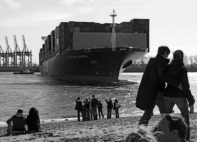 11_21358 das riesige Containerschiff CMA CGM CARMEN wird auf der Hhe des Standcafs "Strandperle" mit Hilfe von Schleppern auf der Elbe gewendet und rckwrts in den Waltershofer Hafen gebracht. Im Hintergrund sind die Containerbrcken vom Container Terminal EUROGATE zu erkennen. Am Stand stehen Schaulustige und blicken zu dem hohen Bug des Containerschiffs. Der Containerfrachter hat eine Lnge ca. 300m und eine Breite von 40m; das Schiff kann 6627 TEU / 20 Fuss Container als Ladung an Bord nehmen. Das 2006 gebaute Frachtschiff hat eine Hchstgeschwindigkeit von 25,2 kn. www.bildarchiv-hamburg.de