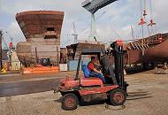 37_5045 Ein Gabelstaplerfahrer fhrt sein Fahrzeug ber das Werftgelnde der Sietaswerft. Im Hintergrund Stahlsegmente eines Schiffsneubaus. 