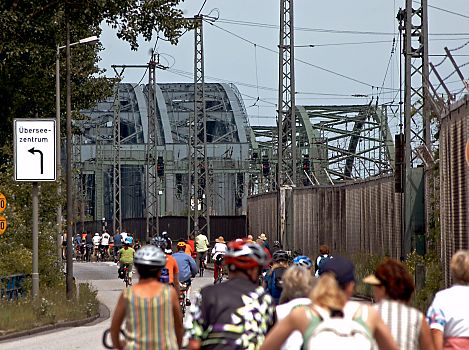 011_17398 - FahrradfahrerInnen, teilweise mit Helm, fahren entlang des Zollzauns Richtung Freihafen Elbbrcke. Ein Strassenschild weist die Richtung zum berseezentrum. 