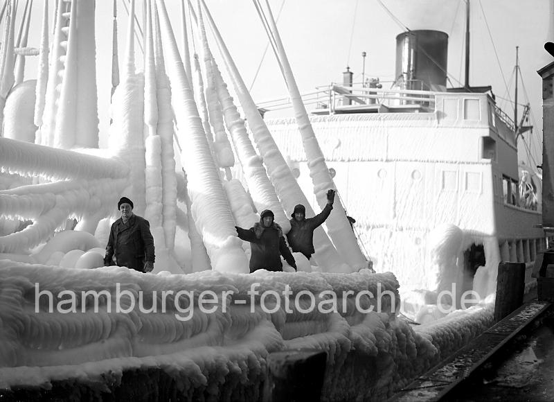 219_8_83 Die Mannschaft eines norwegischen Frachters, der garade im Hambuger Hafen eingetroffen ist, steht an Deck des stark mit Eis bedeckten Schiffs. Die Decksaufbauten und Takelage des Frachtschiffs sind mit einer sehr dicken Eisschicht berzogen. Winter im Hamburger Hafen - vereister Frachter; Eisschicht an Deck + Takelage; ca. 1934.