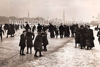 1086_3505_51 Kinder mit ihren Mttern auf dem Eis der zugefrorenen Aussenalster - einige haben Schlittschuhe untergeschnallt, andere glitschen auf dem Eis. Im Hintergrund Kirchtrme der Hansestadt Hamburg. 