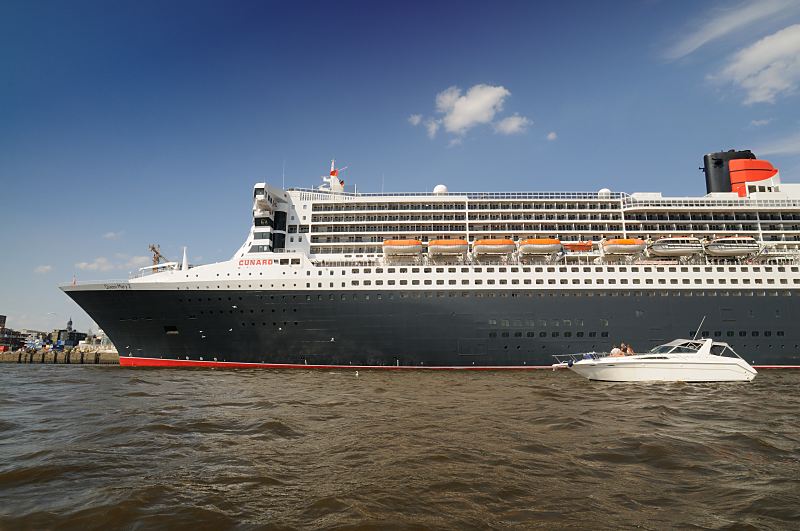 Das Passagierschiff Queen Mary 2 in Hamburg, Seitenansicht - Rettungsboote. 05_4350 Die Queen Mary 2 am Kreuzfahrtterminal im Hamburger Hafen; unter dem Bug ist die St. Michaelis Kirche zu erkennen. Die R.M.S. (Royal Mail Ship)  Queen Mary 2 (QM2) ist mit 148.528 BRZ eines der grten Passagierschiff der Welt. Das britische Kreuzfahrtschiff  hat eine Lnge von 345 m und eine Breite von 45 m. Der Luxusliner bietet in 1310 Kabinen bis zu 2.620 Passagieren Platz und hat eine Besatzung von 1.253 Personen.  Durch den 157.000 PS starken, aus vier Dieselmotoren und Zwillingsgasturbinen bestehenden Antrieb erreicht das Schiff eine Geschwindigkeit von 30 Knoten (ca. 56 km/h) und hat einen Tiefgang von nur 10m.Die Queen Mary 2 hat fnf Swimmingpools, einen Ballsaal, Golfanlage, Wintergarten, Sportzentrum, mit ber 8.000 Bchern die grte Bibliothek auf See, den grten ffentlichen Saal (Restaurant Britannia), der ber zwei Decks und die gesamte Schiffsbreite geht, acht weitere Restaurants, Fitness-Center, Planetarium, Kino, Theater. www.fotograf-hamburg.de