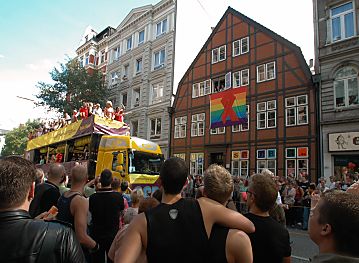 011_14675 - Christopher Street Day (CSD) Parade in der Langen Reihe; Regenbogenfahne mit dem Red Ribbon, das die Solidaritt mit AIDS betroffen ausdrckt, am Fachwerkhaus.Ein schwules Paar steht an der Strae und beobachtet den vorbeifahrenden Fest - Truck.